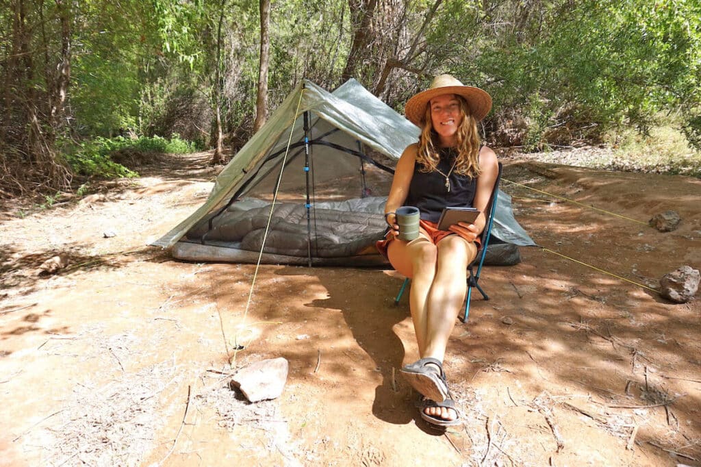 Woman sitting on Helinox Chair Zero camp chair in front of Zpacks duplex tent at campsite