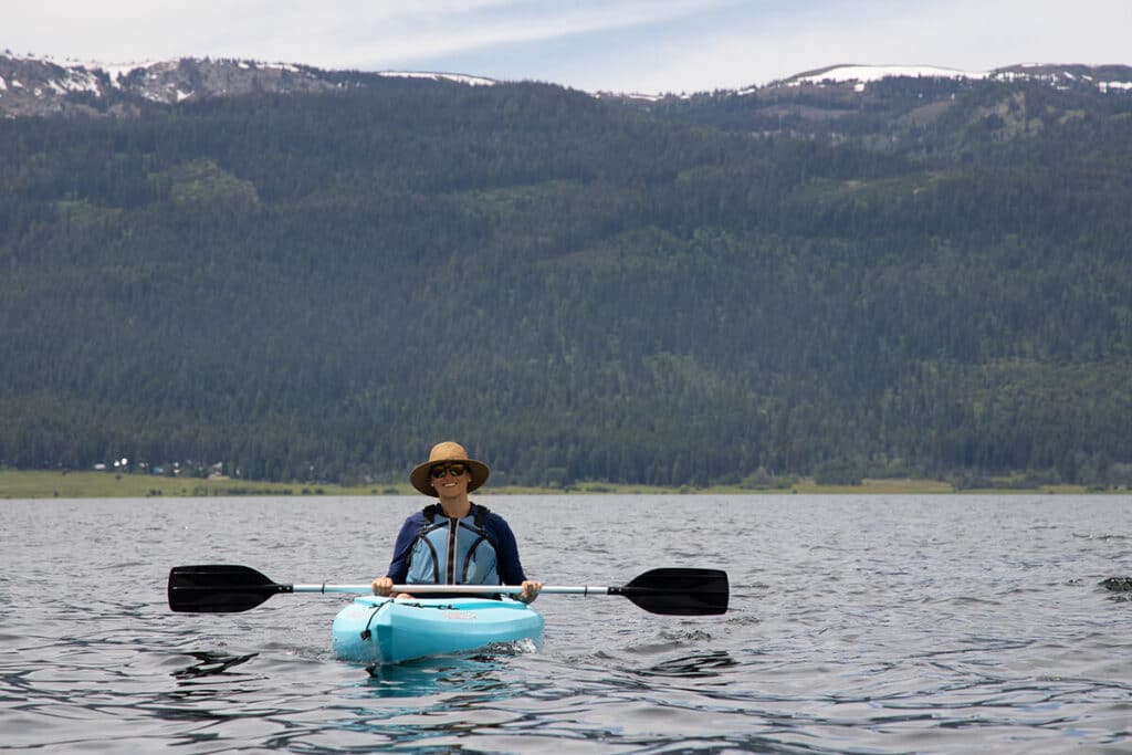 Woman kayaking wearing a life vest (PFD) with forested mountains in the background