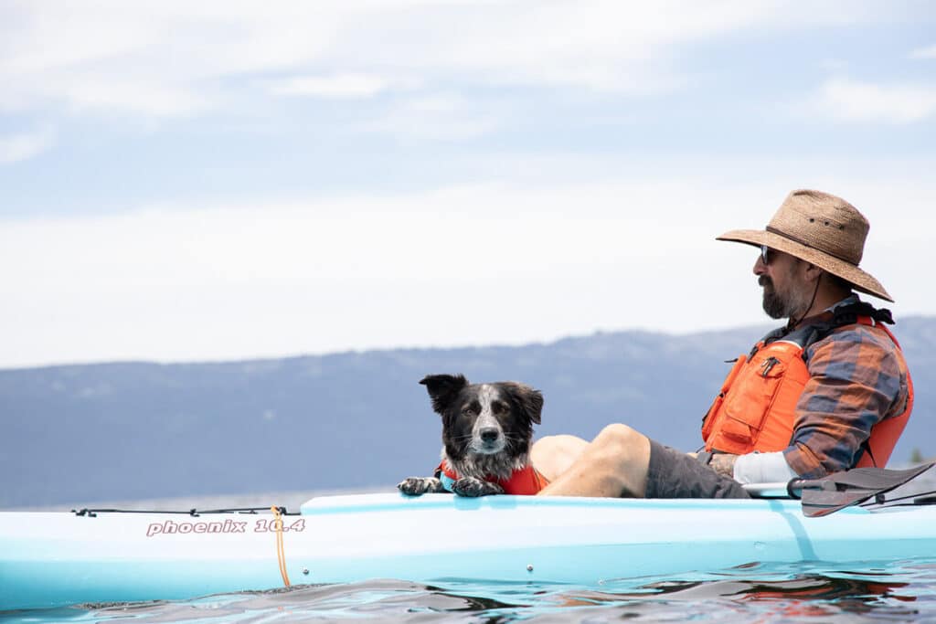 Man and dog sitting in a kayak with distant mountains in the background