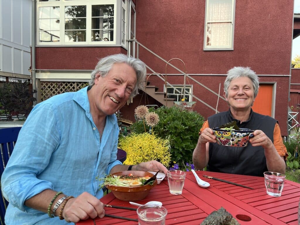 two people sitting at a table in a backyard eating dinner