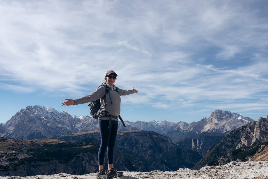 A woman stands with her arms outstretched hiking on the Cortina d Ampezzo Tre Cime Circuit 25 in Italy wearing Patagonia Cool Capilene Hoodie