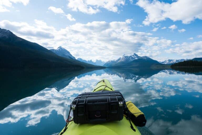 Front of green kayak on Maligne Lake in Alberta. The mountains and clouds are reflected on the perfectly still water