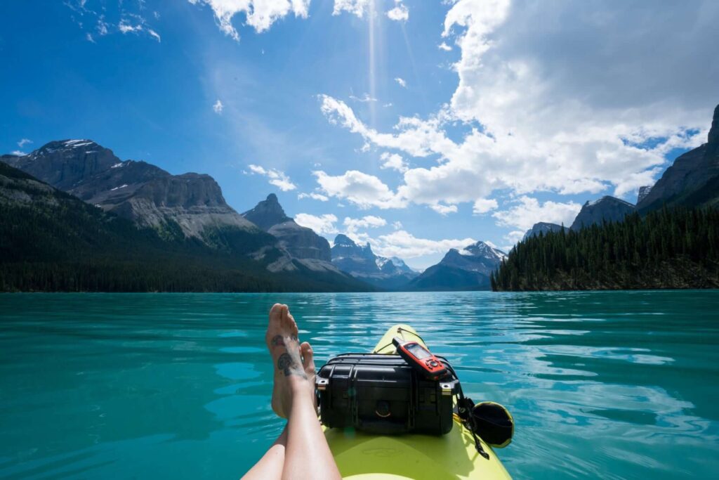 Woman's feet resting on bow of kayak on turquoise Lake Maligne in Alberta surrounded by snow-capped peaks