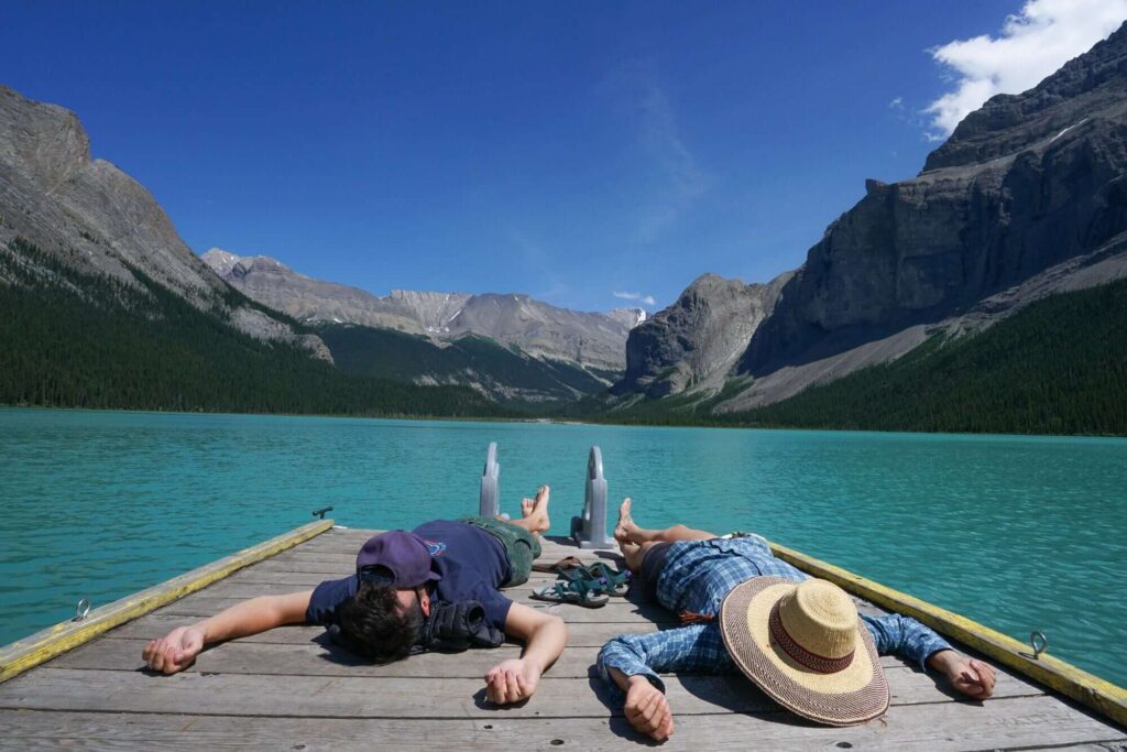 Two people laying on their backs on dock on Lake Maligne surrounded by tall rocky cliffs