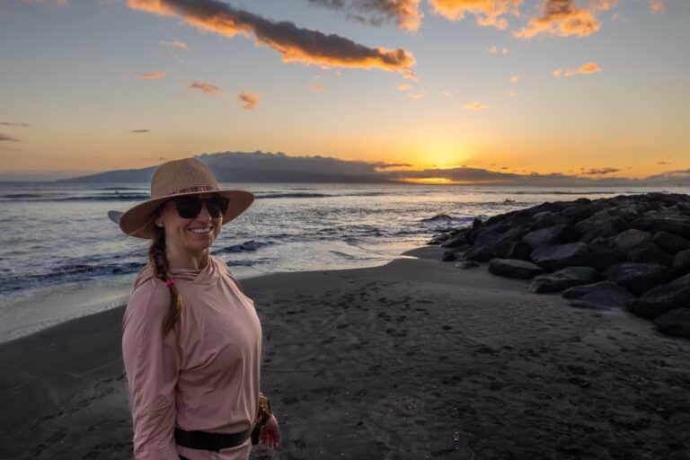 Kristen Bor standing on the beach in Maui at sunset wearing a pink REI Sahara Shade Sun Protection Hoody