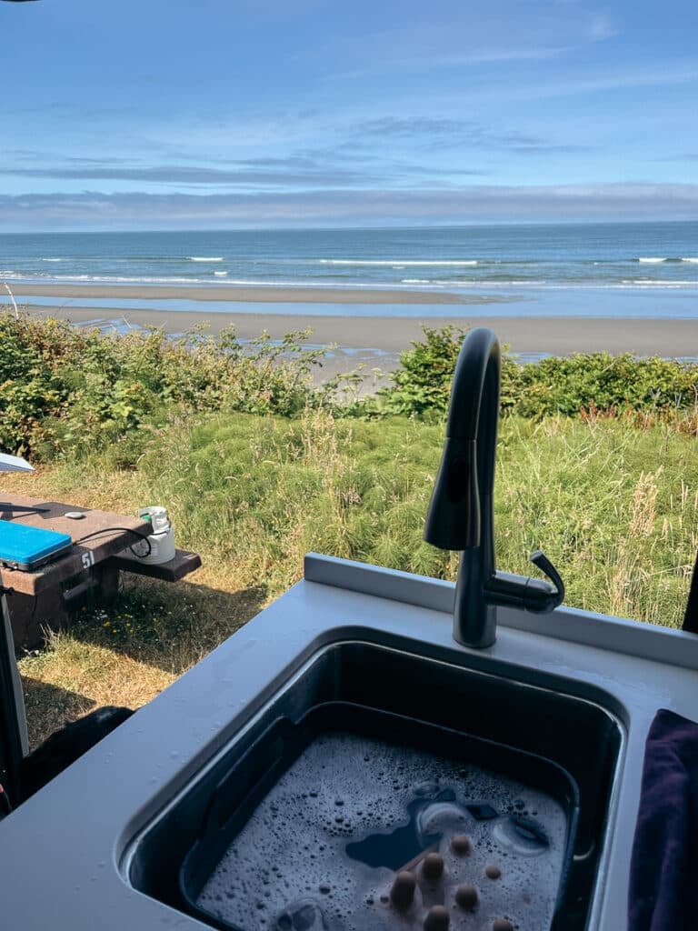 The view from the kitchen inside of a Sprinter Van parked on a cliff above the ocean at South Beach campground in Olympic National Park