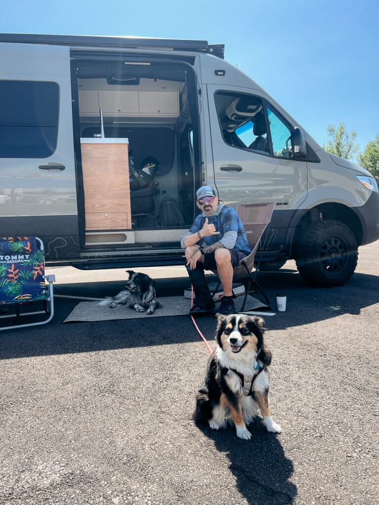 A man and a mini australian shepherd sitting in front of a Sprinter Van