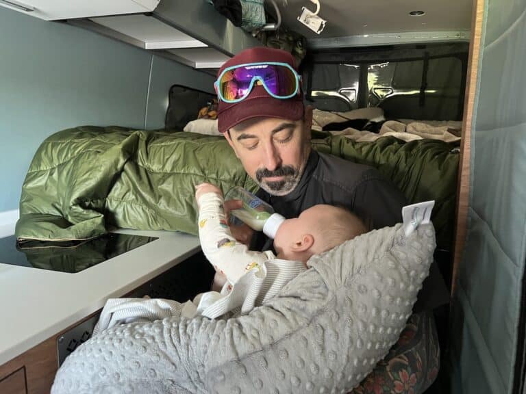 A man feeding an infant in a Sprinter Van