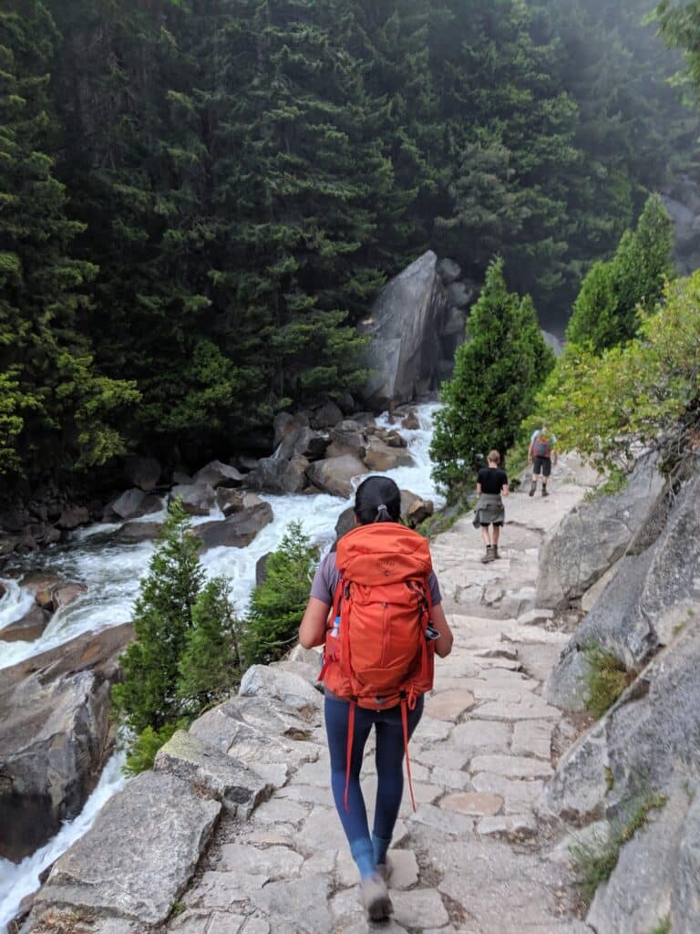 A woman hiking to Half Dome wearing a red backpack