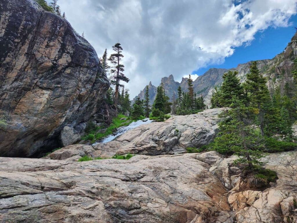 Small waterfall cascading down rocks in Rocky Mountain National Park with tall mountains as backdrop