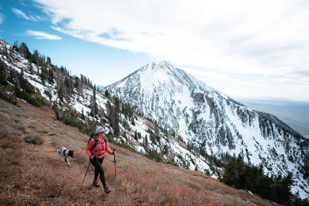 Woman hiking with dog on mountain in Colorado with snowy peaks on next ridge