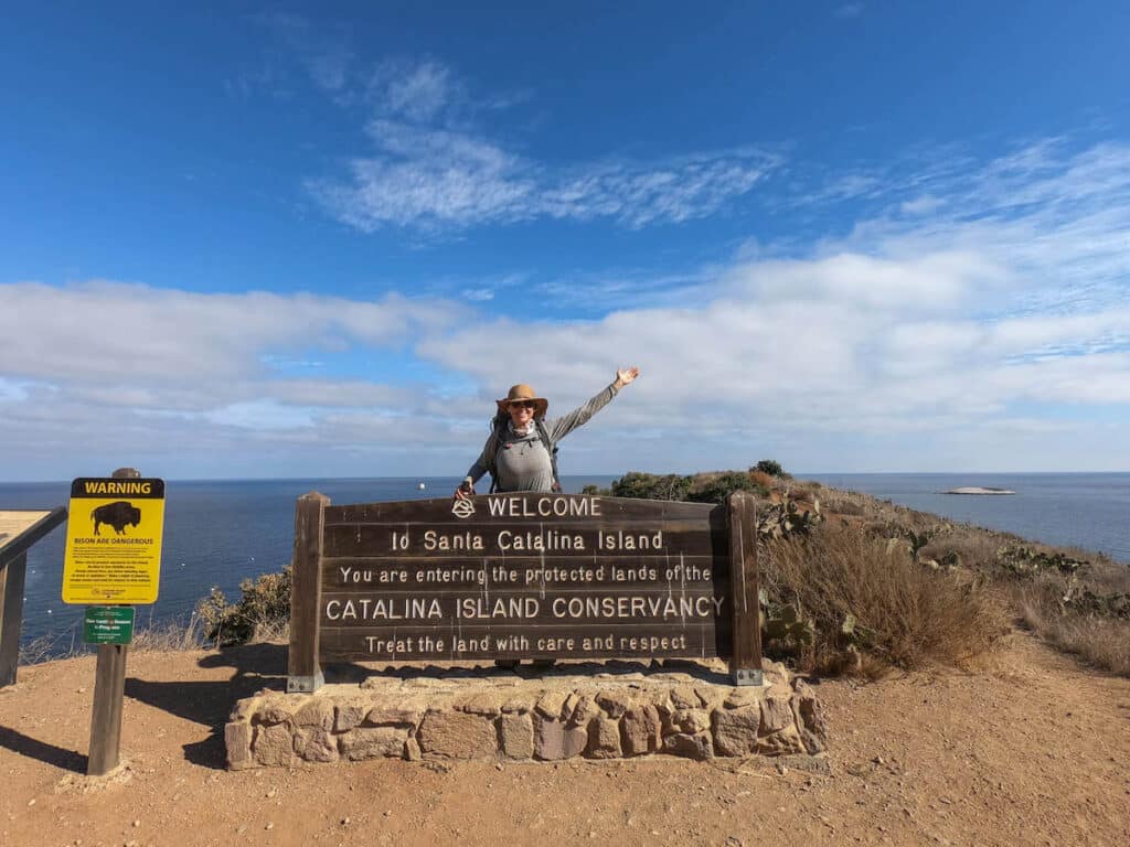 Woman standing overdue large welcome sign that says "welcome to Santa Catalina Island. You are inward the protected lands of the Catalina Island Conservency. Treat the land with superintendency and respect"