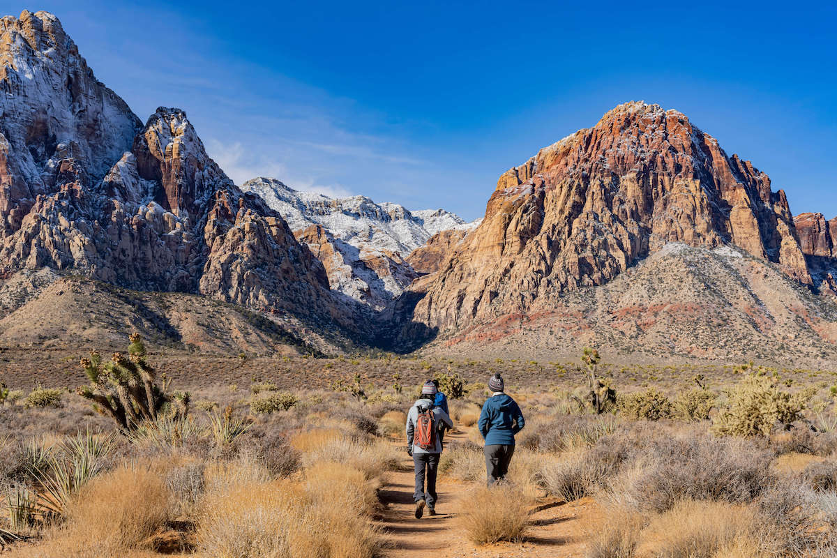 Hikers on Las Vegas hiking trail leading to canyon with snow-dusted mountains in the distance