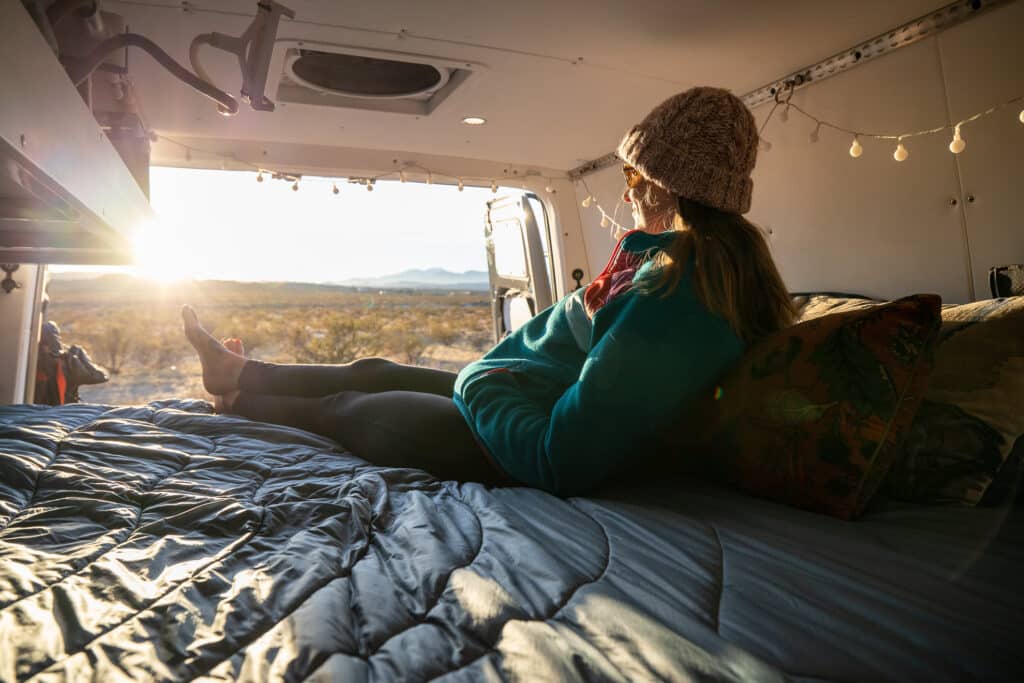 Kristen Bor lying in the back of her Sprinter Van in Joshua Tree with a view of the sunset wearing the Cotopaxi Teca Fleece