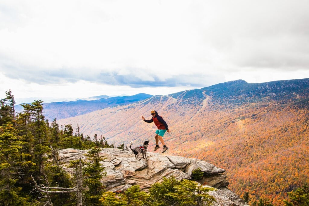 Man jumping in air on a rock with fall foliage in the background