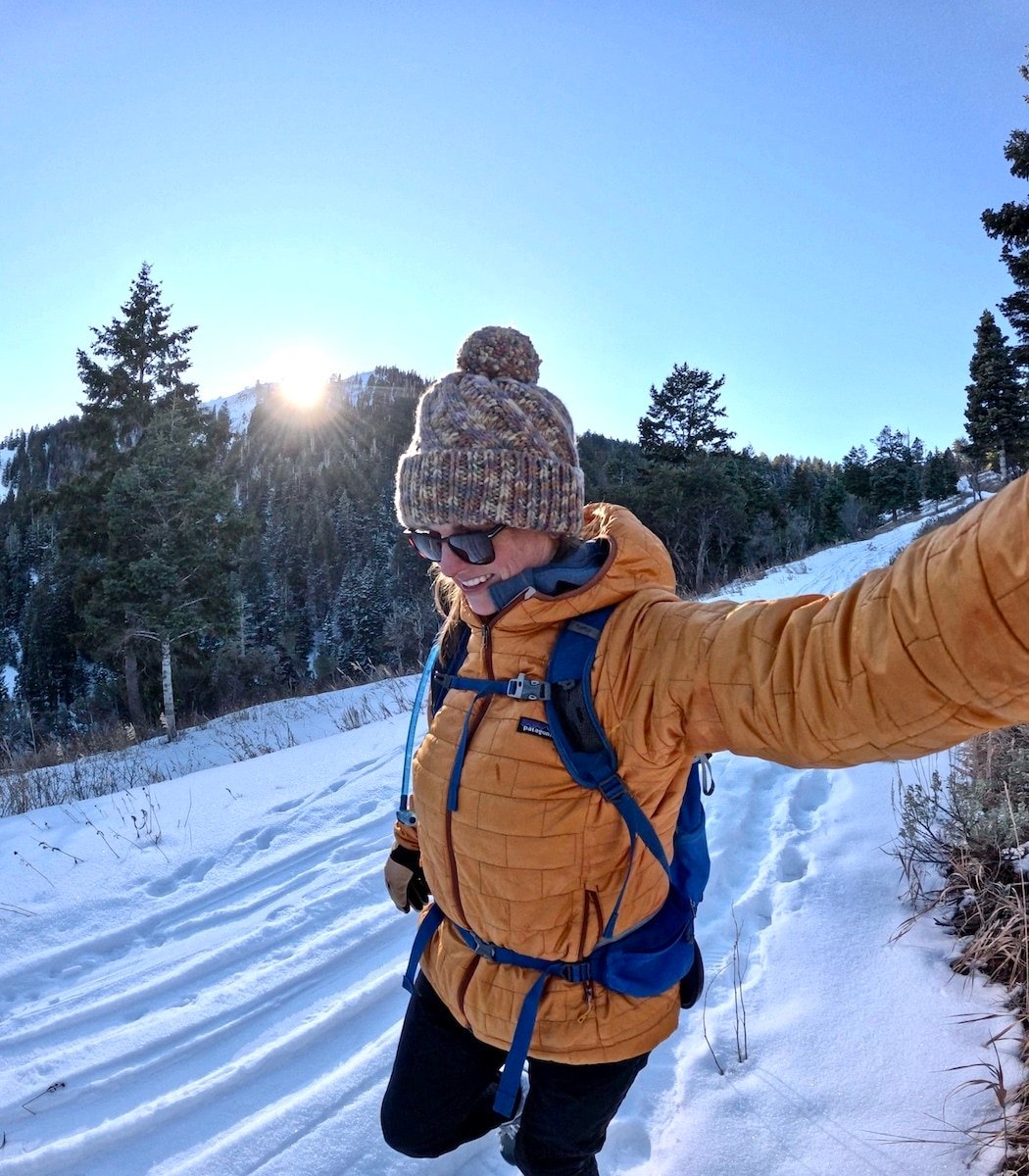 BFT Founder Kristen smiling in a golden yellow Patagonia Nano Puff and beanie on a snowy hike in Utah