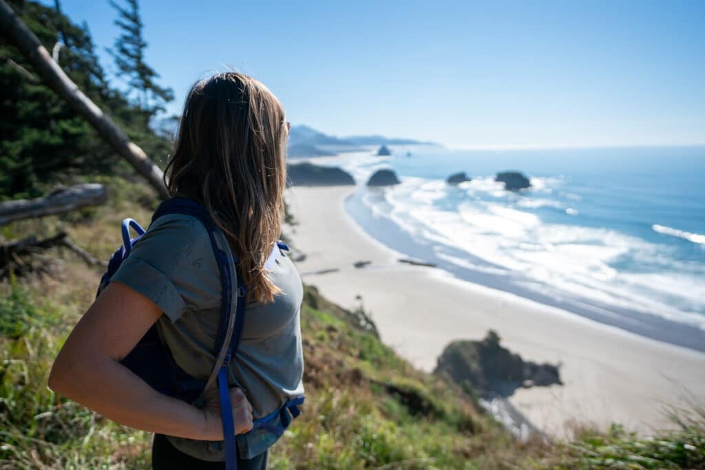 Woman standing on the edge of an overlook looking down at a sandy beach at Ecola State Park in Oregon