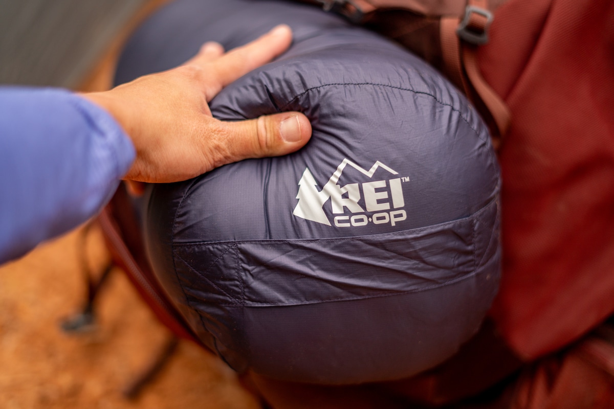 A hand pulling out the REI Magma sleeping bag from a backpack 