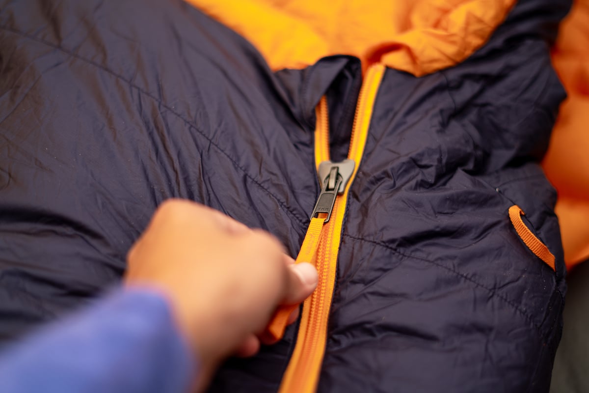 A hand pulling the zipper on the REI Magma sleeping bag