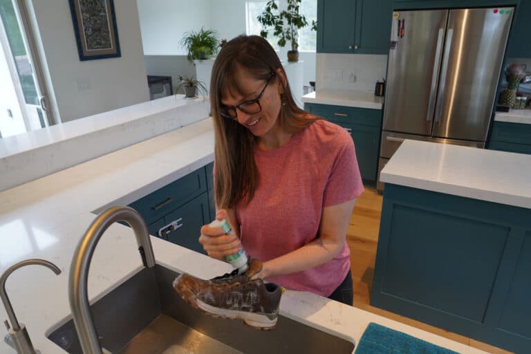 Kristen Bor cleaning hiking boots over kitchen sink with Nikwax footwear cleaning gel