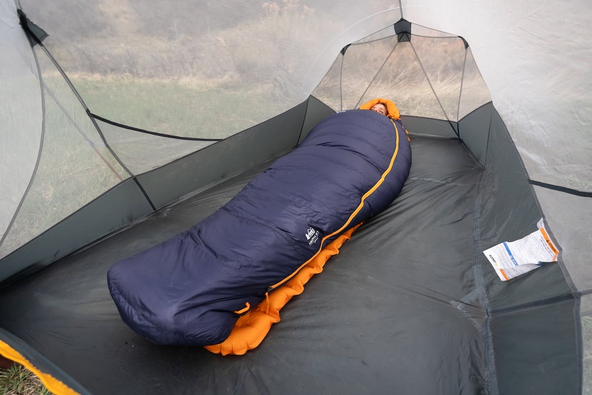 Woman laying down in the REI Magma sleeping bag on a sleeping pad inside of a tent