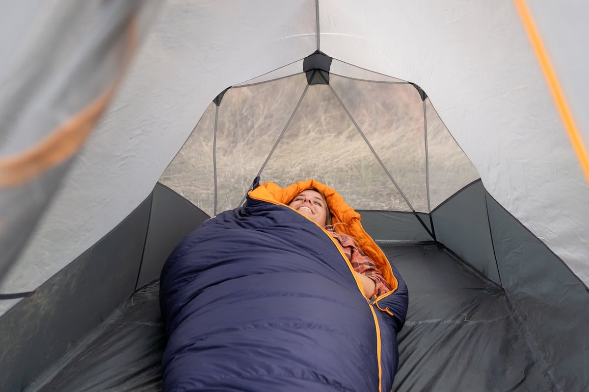 A woman laying down in the REI Magma sleeping bag in a tent and smiling