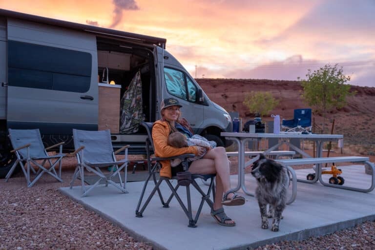 Kristen Bor sitting in a camp chair holding baby at a campsite at Roam Horseshoe Bend RV Resort next to a Sprinter Van