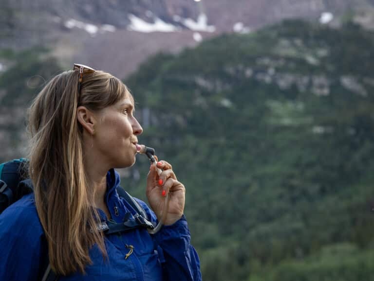 a closeup of Kristen Bor drinking water from a hydration reservoir with mountains in the background