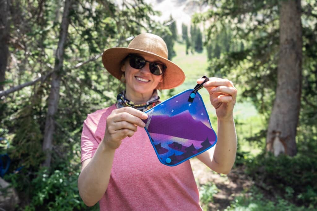 Kristen Bor holding Kula Cloth pee rag featuring a bear next to a lake with a cosmic mountain scene