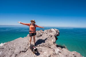 Kristen Bor standing on a cliff on the ocean wearing hiking clothes and a backpack