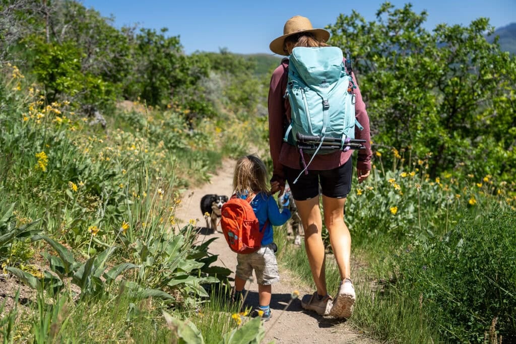 Kristen Bor wearing the Deuter Trail 28 SL backpack on a trail in Park City with green foliage next to her 2 year old son