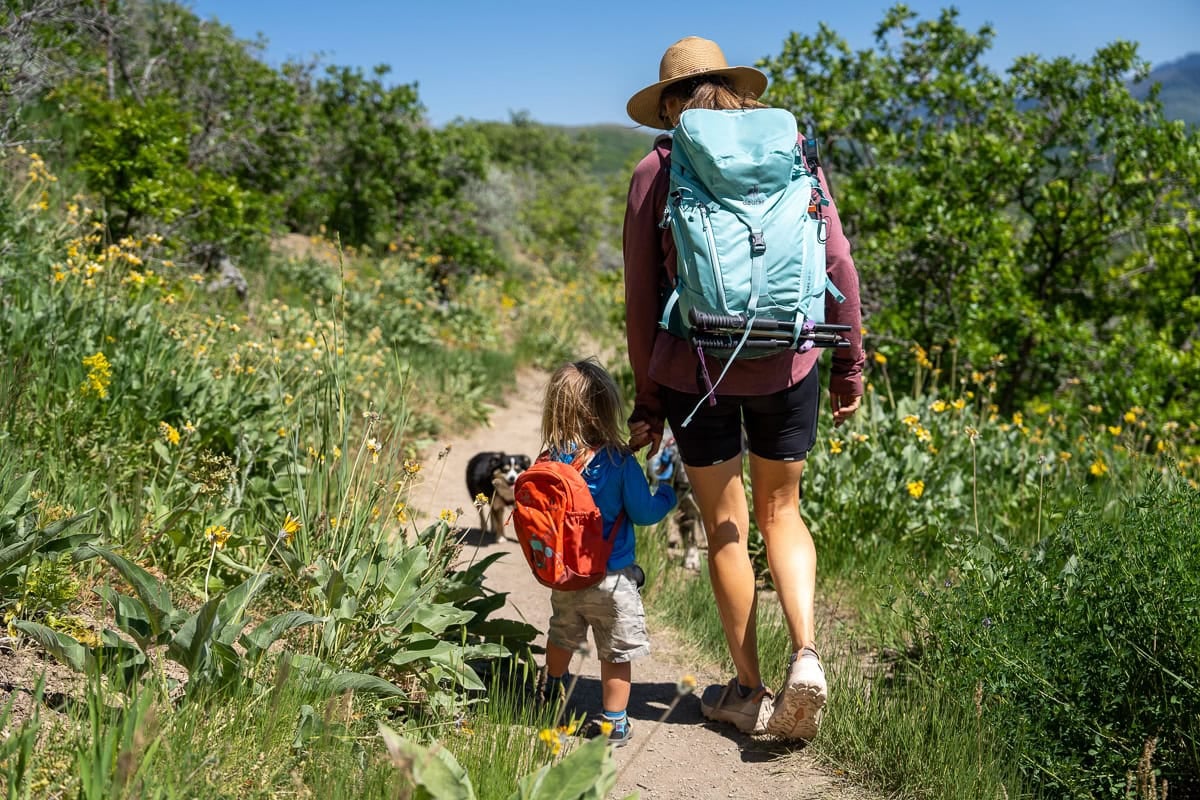 Kristen Bor wearing the Deuter Trail 28 SL backpack on a trail in Park City with green foliage next to her 2 year old son