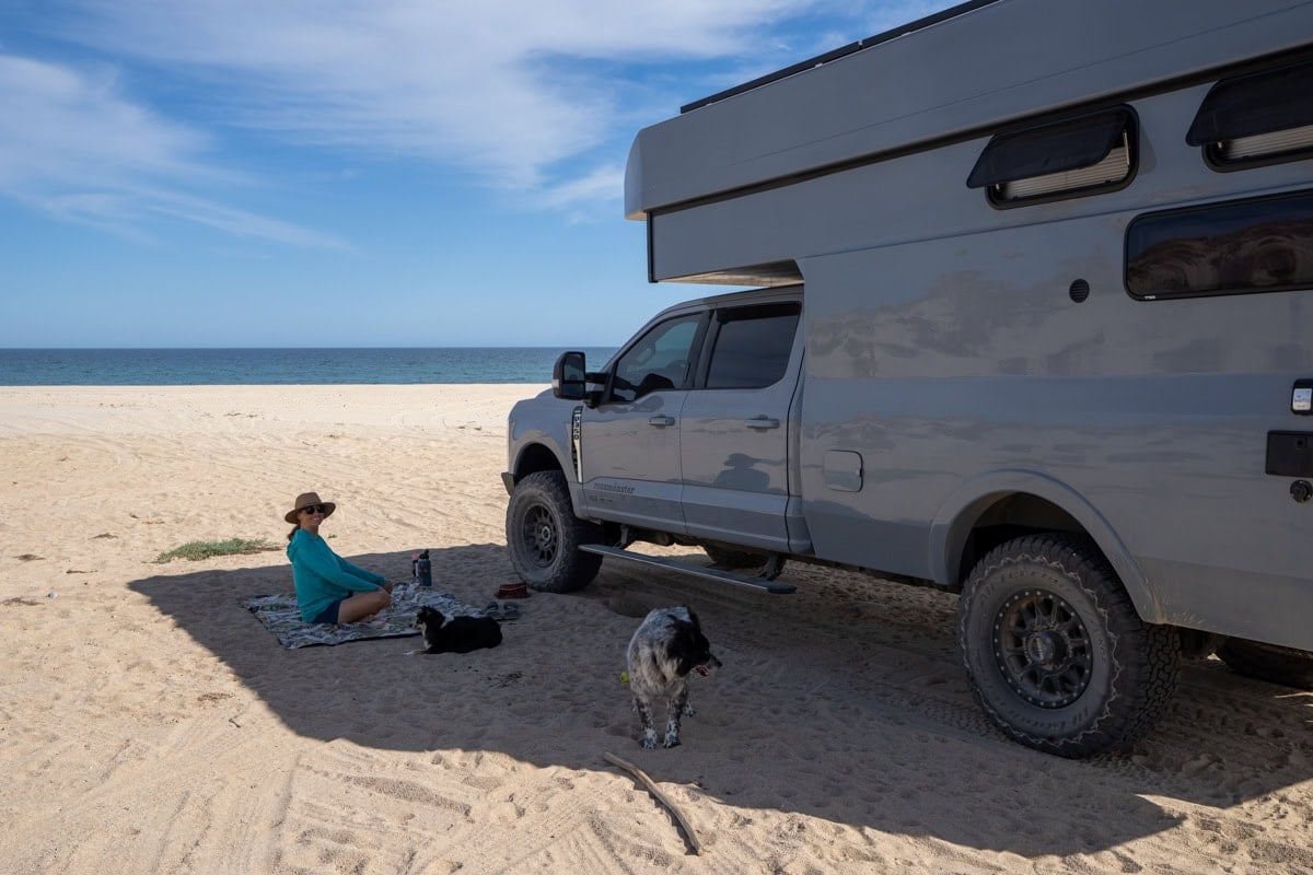 Kristen Bor sitting next to the Rossmonster Baja Trail LX on a beach in Baja next to the ocean