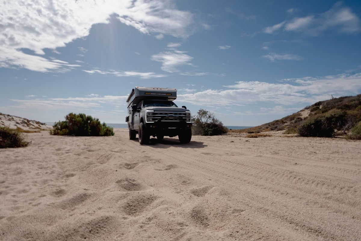 Rossmonster Baja Trail LX adventure truck camper driving on a dirt road with the ocean in the background in Baja