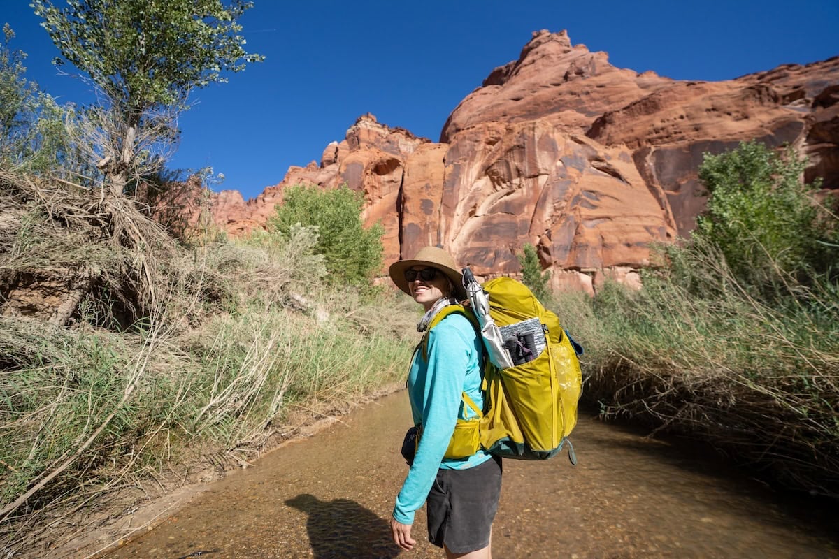 Kristen Bor standing in a river in Paria Canyon with a backpacking pack on