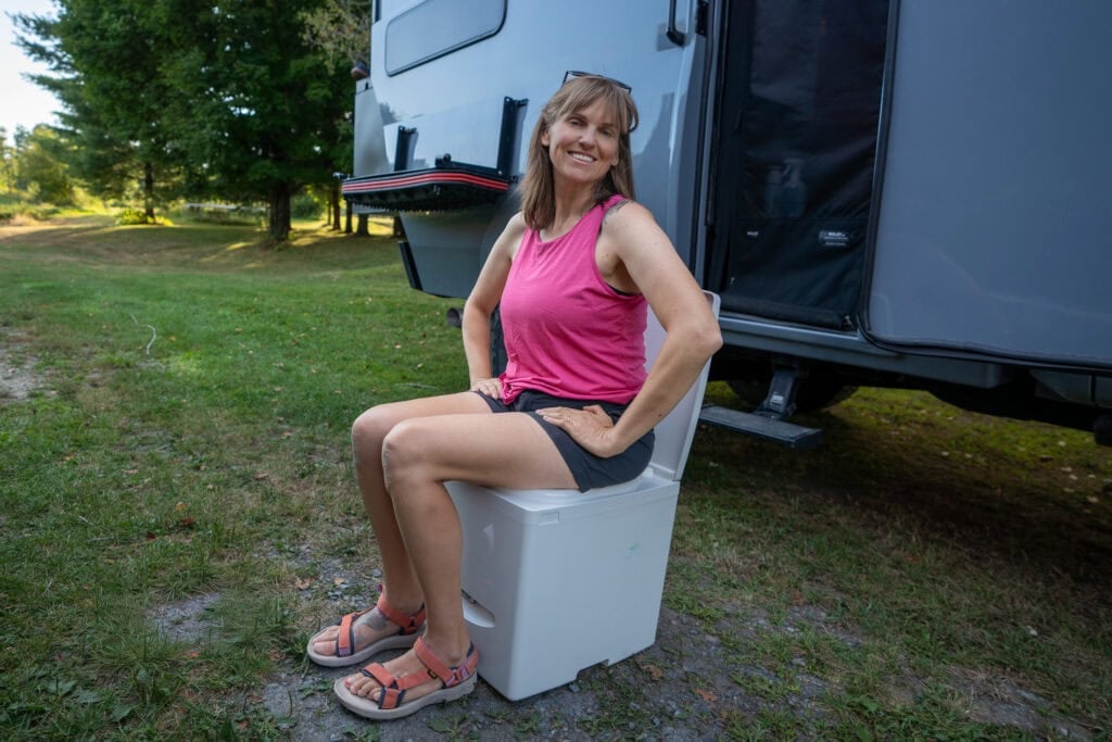 Kristen Bor demonstrating how to use the Compocloset Cuddy Lite composting toilet standing in front of a truck camper
